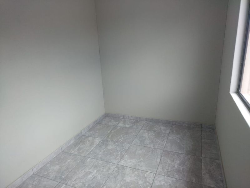 A clean, empty room featuring neutral wall paint and modern grey tiled flooring, suitable for use as a bedroom or home office.