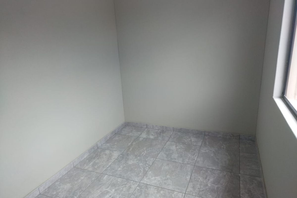 A clean, empty room featuring neutral wall paint and modern grey tiled flooring, suitable for use as a bedroom or home office.