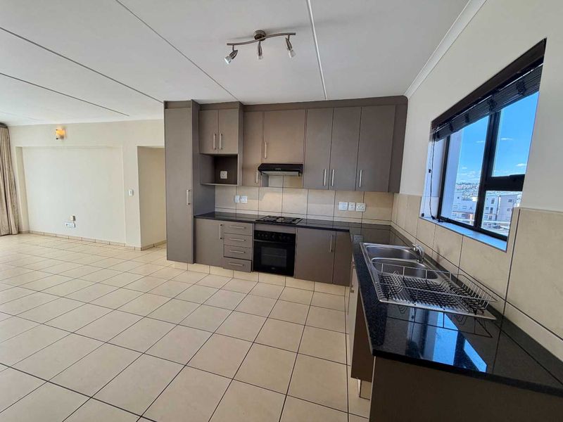 An open-plan kitchen featuring modern grey cabinetry, granite countertops, built-in oven, gas hob, and tiled flooring, offering a clean and functional living space.