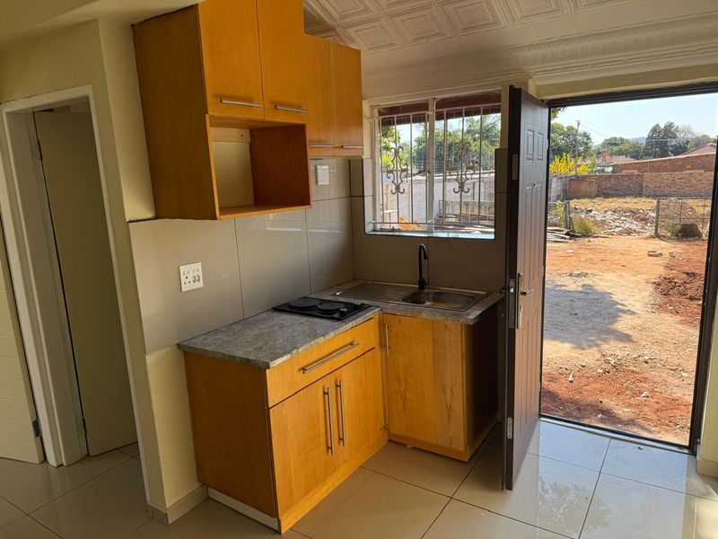Compact kitchen featuring wooden cabinetry, laminate countertops, an electric hob, and direct access to the exterior through a side door.