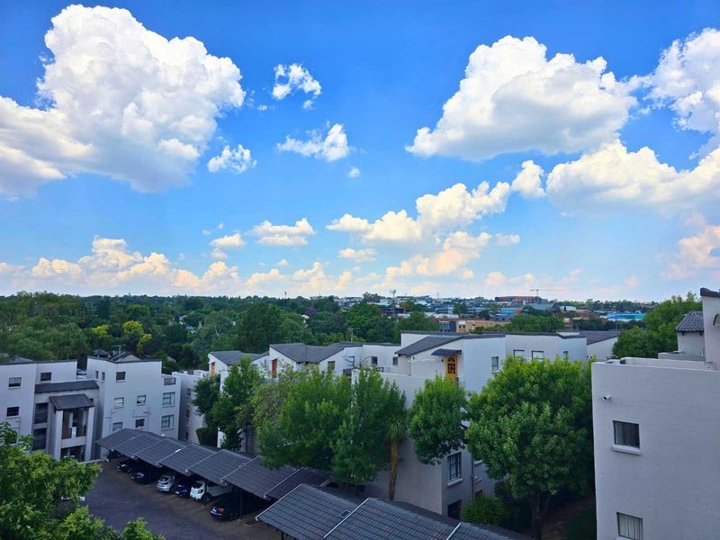 Elevated view overlooking the apartment complex grounds, featuring established trees and covered parking bays under a clear blue sky.