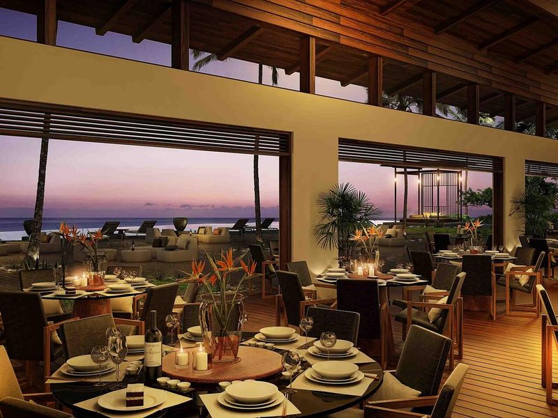 Expansive covered outdoor dining area featuring timber decking, exposed beam ceilings, and seamless transition to a scenic oceanfront patio.