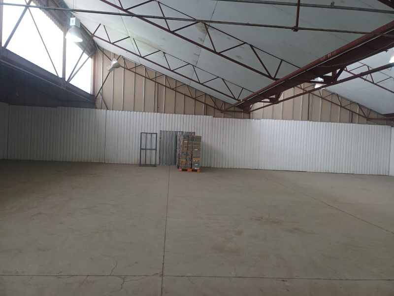 Spacious industrial warehouse unit featuring high ceilings with exposed steel trusses, corrugated metal walls, and durable concrete flooring.