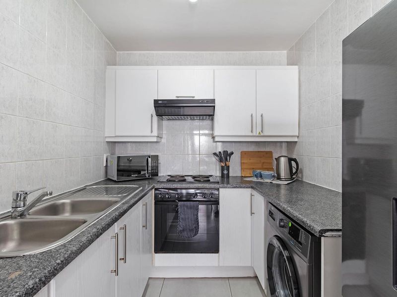 Compact kitchen featuring white cabinetry, granite-look laminate countertops, tiled backsplash, and integrated oven with extractor fan.