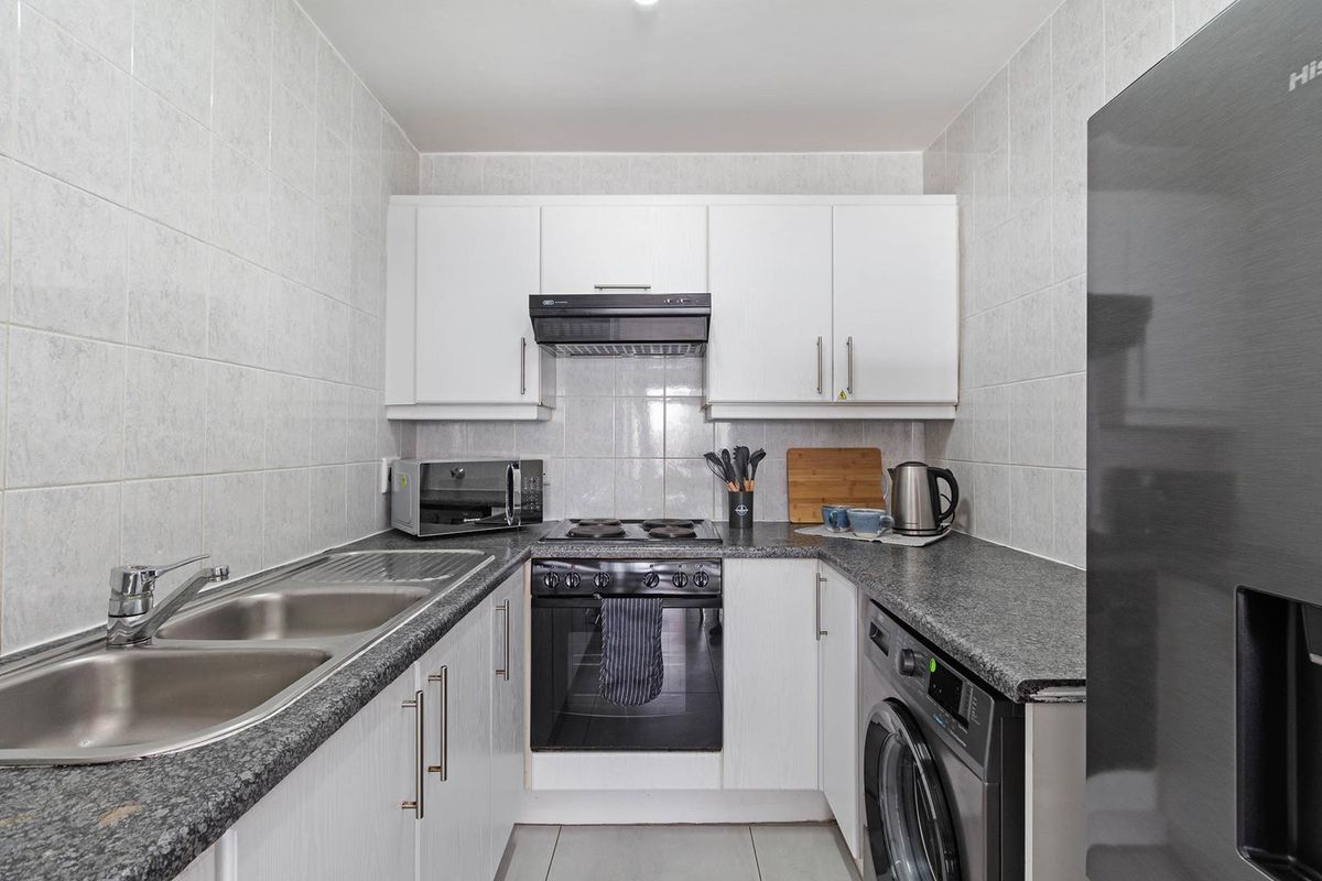 Compact kitchen featuring white cabinetry, granite-look laminate countertops, tiled backsplash, and integrated oven with extractor fan.