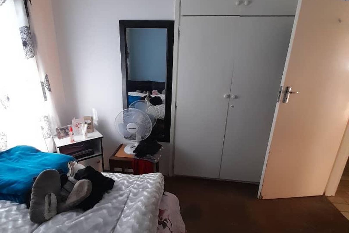 A functional bedroom featuring built-in cupboards and carpeted flooring, offering a practical layout with natural light.