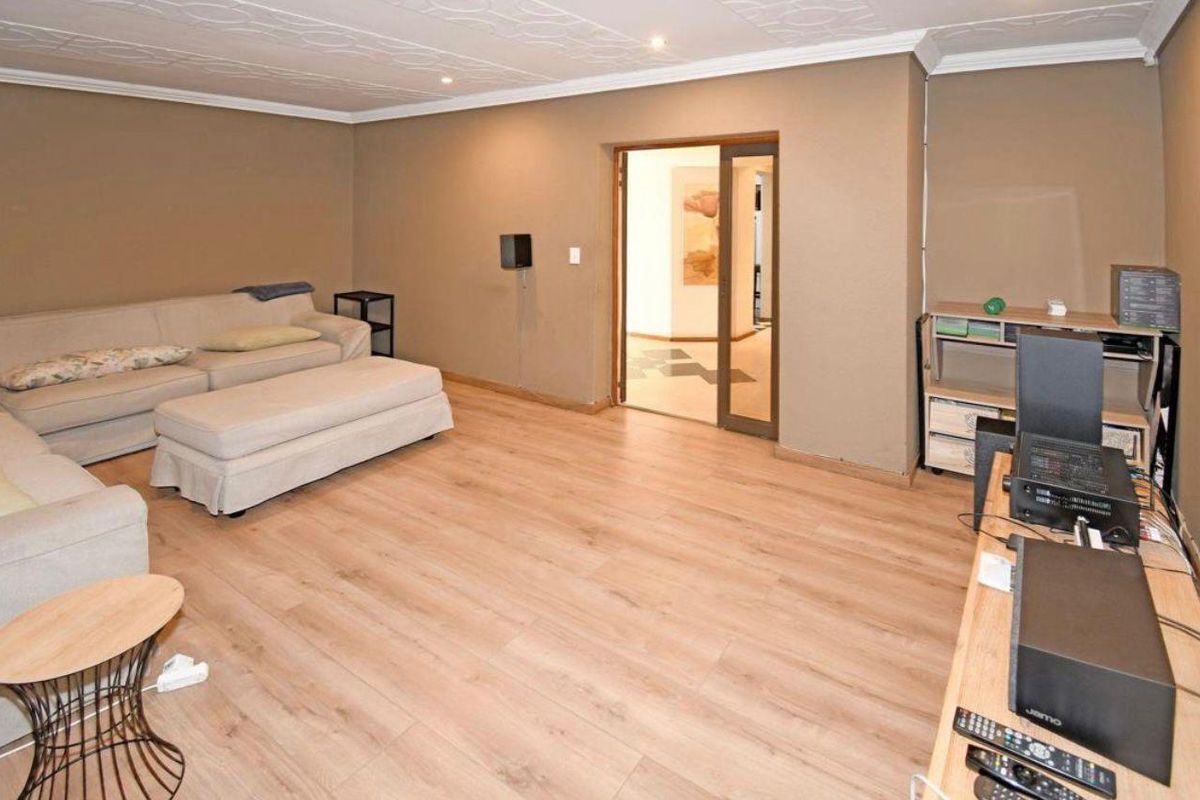 A living room featuring light-toned laminate flooring, a textured ceiling with recessed lighting, and a sliding door leading to an adjacent space.