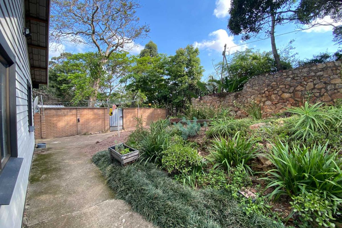 A private rear garden area featuring a concrete pathway, landscaped terraced garden beds, and secure brick boundary walls with perimeter fencing.