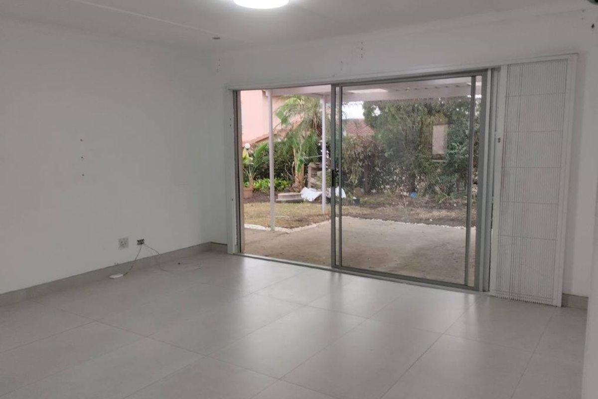 An empty, light-filled living room featuring large sliding glass doors that open directly onto a rear patio and garden area.