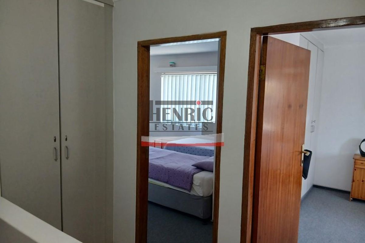 A bedroom interior featuring built-in cupboards and timber door frames, viewed from an adjacent hallway.