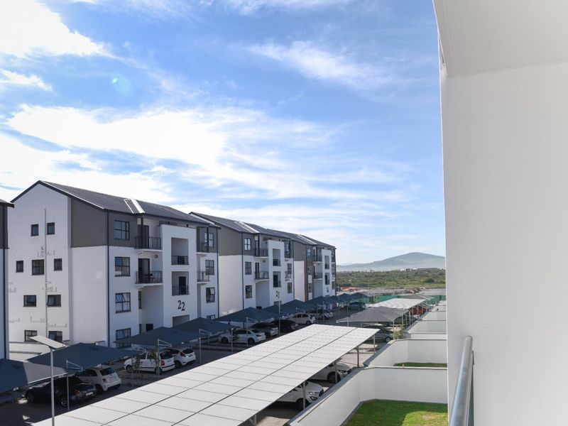 Elevated view from a balcony overlooking the apartment complex grounds, featuring covered parking bays and surrounding landscape.