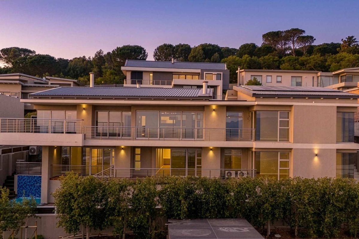 A modern multi-level residential property featuring expansive balconies, large sliding glass doors, solar panels, and a private swimming pool at dusk.