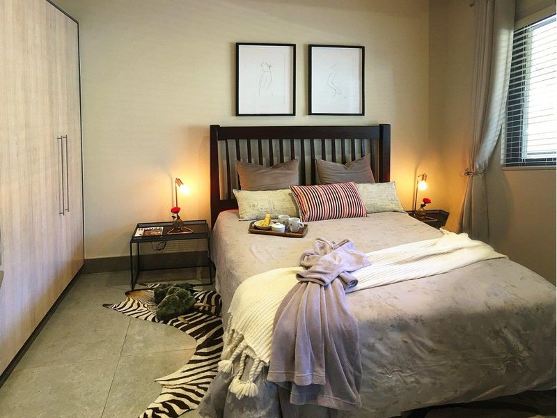 A well-maintained bedroom featuring neutral tiled flooring, a large built-in wardrobe, and venetian blinds for privacy.