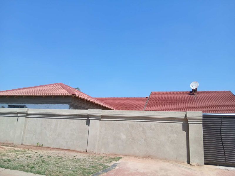 Front exterior view of the property featuring a concrete perimeter wall, tiled roof, and metal gate, with some unfinished plaster work visible.
