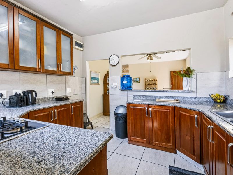 Functional kitchen featuring wooden cabinetry, granite countertops, a gas hob, and a convenient pass-through window connecting to the adjacent living area.