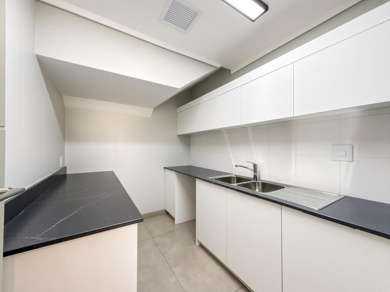 A modern, minimalist kitchen featuring sleek white cabinetry, dark stone countertops, and a stainless steel double sink in a clean, well-lit space.