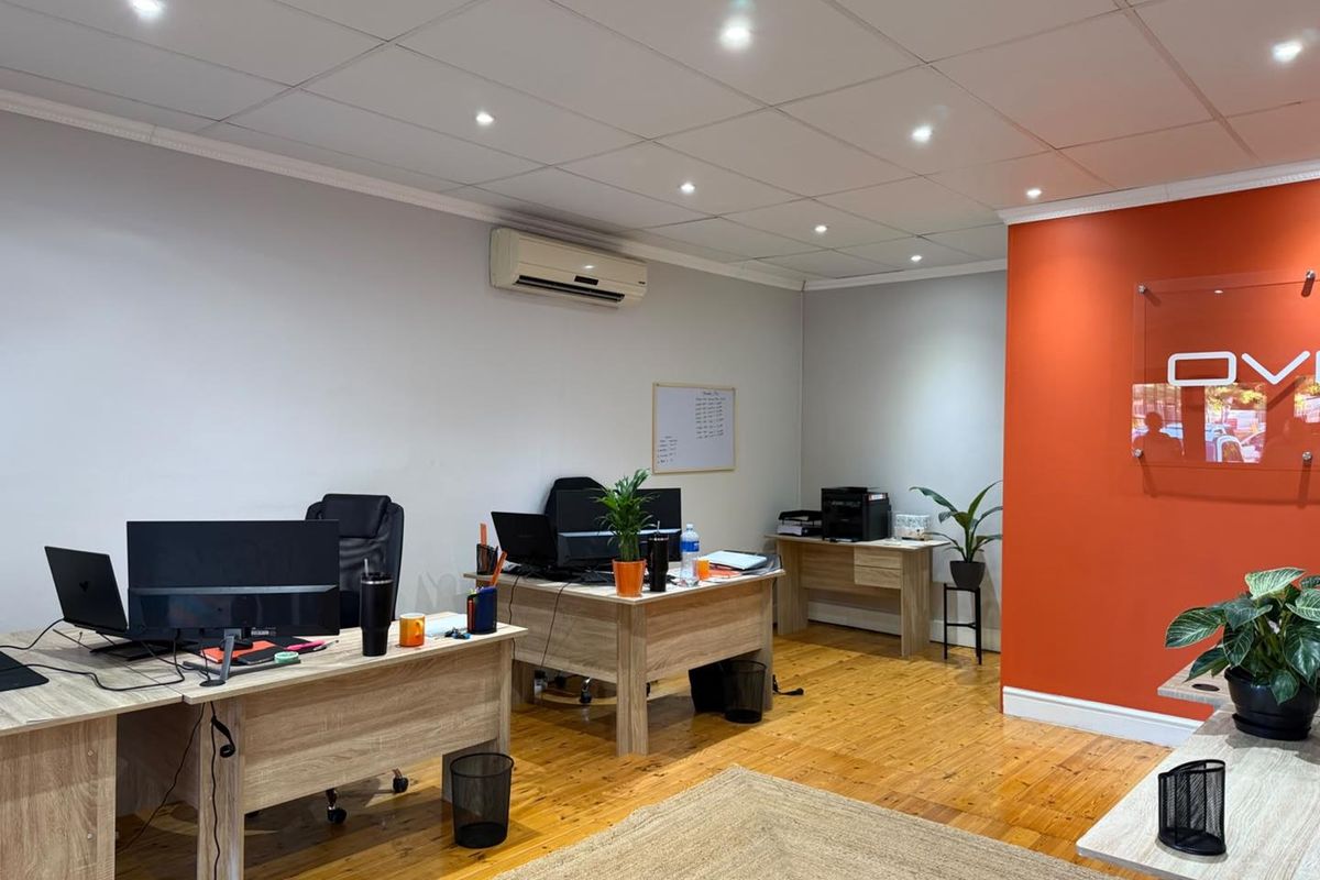 A functional office space featuring hardwood flooring, a suspended ceiling with recessed lighting, and a wall-mounted air conditioning unit.