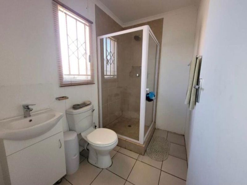 A functional bathroom featuring a shower enclosure, vanity basin, and toilet with tiled flooring and security bars on the windows.