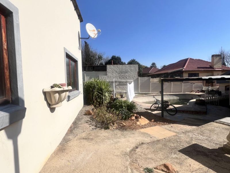 Rear exterior view of the cottage featuring a swimming pool, concrete patio area, and boundary walling.