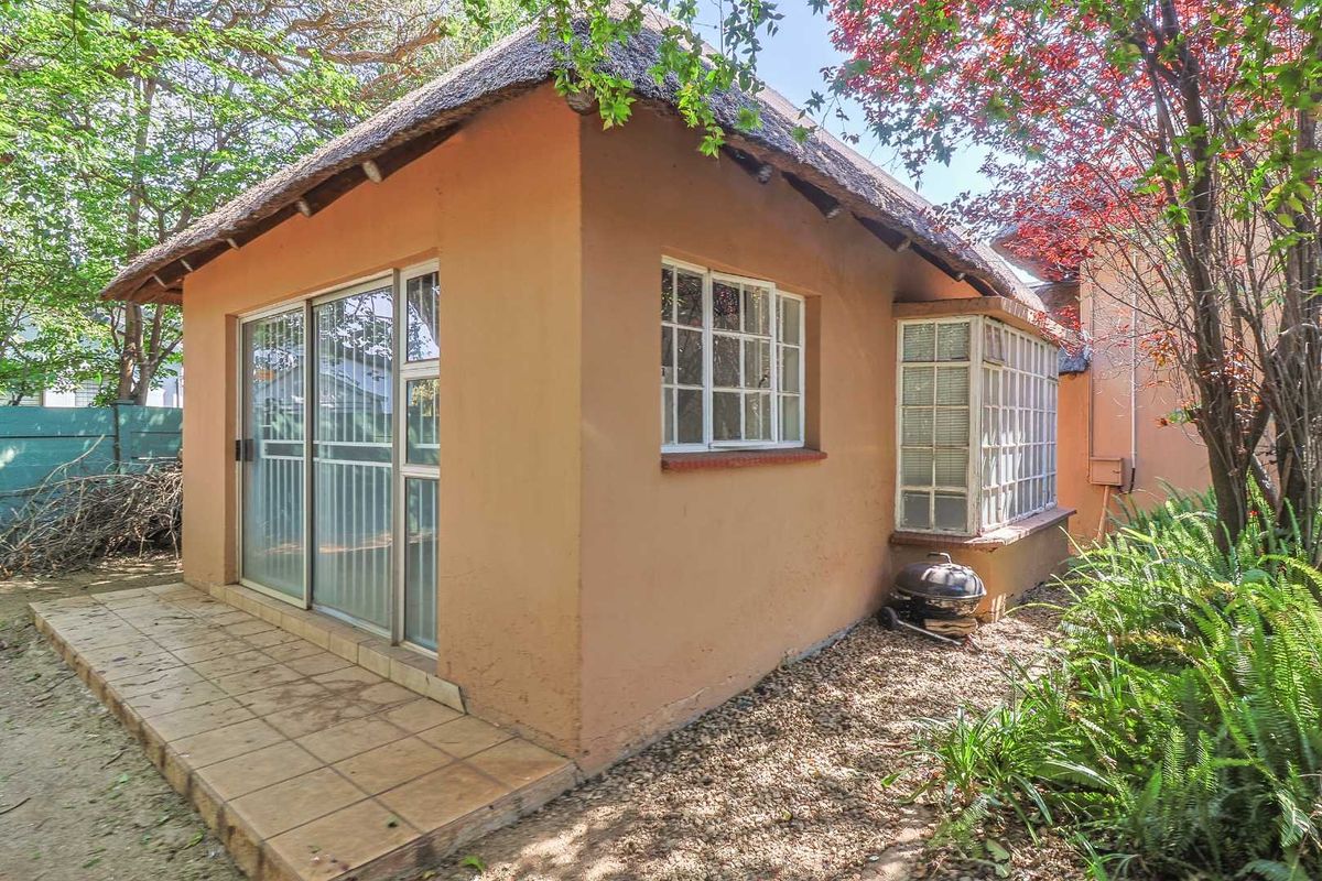 Exterior view of a cottage featuring a thatched roof, tiled patio area, and large sliding glass doors set within a garden environment.