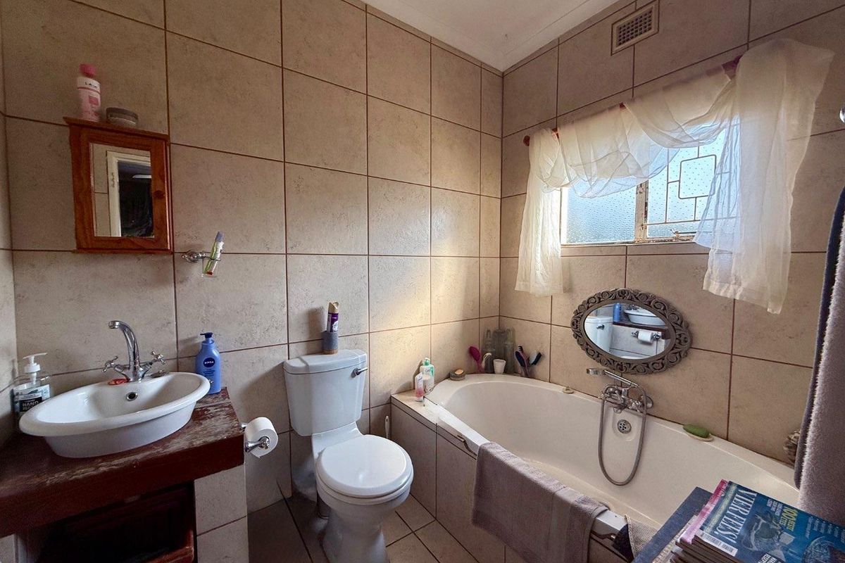 A functional bathroom featuring a built-in bathtub, a ceramic basin with a vanity, a toilet, and floor-to-ceiling wall tiling.