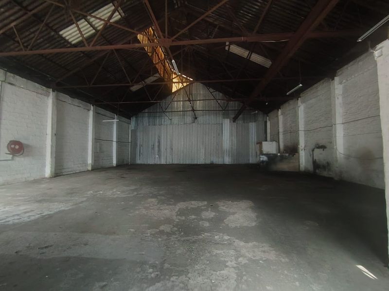 Spacious industrial warehouse unit featuring high ceilings with exposed steel trusses, concrete flooring, and corrugated metal wall cladding.
