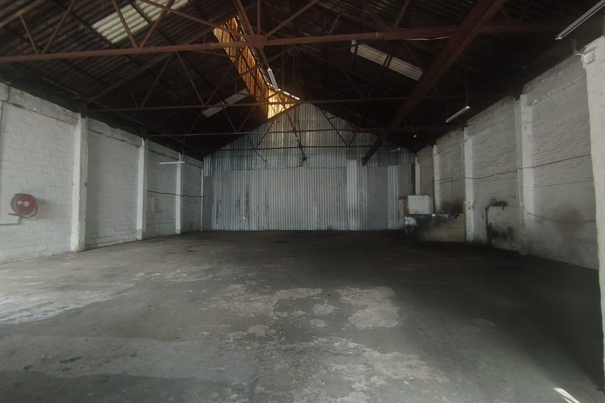 Spacious industrial warehouse unit featuring high ceilings with exposed steel trusses, concrete flooring, and corrugated metal wall cladding.