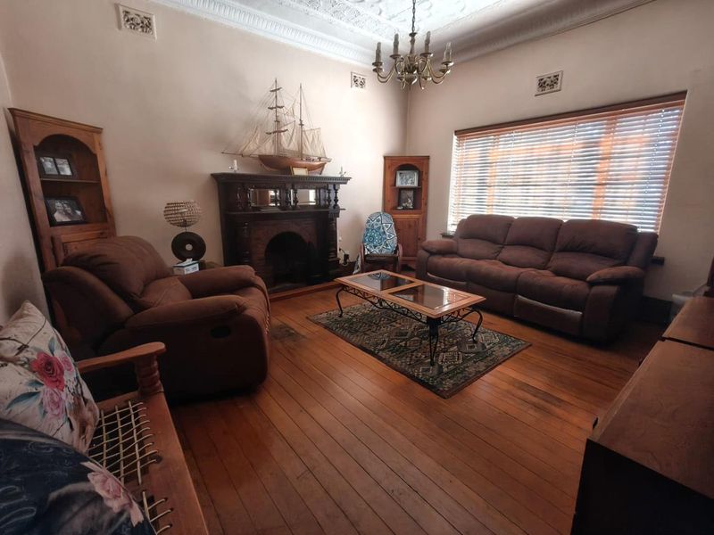 A character-filled living room featuring original timber flooring, an ornate fireplace, decorative ceiling cornices, and built-in corner cabinetry.