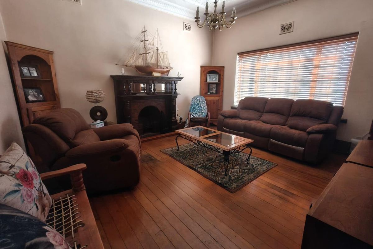 A character-filled living room featuring original timber flooring, an ornate fireplace, decorative ceiling cornices, and built-in corner cabinetry.