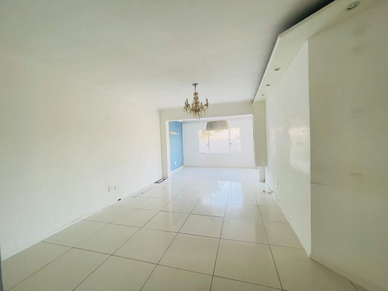 A spacious, empty living area featuring polished tiled flooring, recessed ceiling lighting, and a central chandelier, offering a blank canvas for interior design.