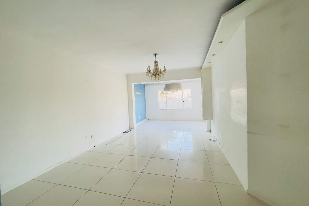 A spacious, empty living area featuring polished tiled flooring, recessed ceiling lighting, and a central chandelier, offering a blank canvas for interior design.