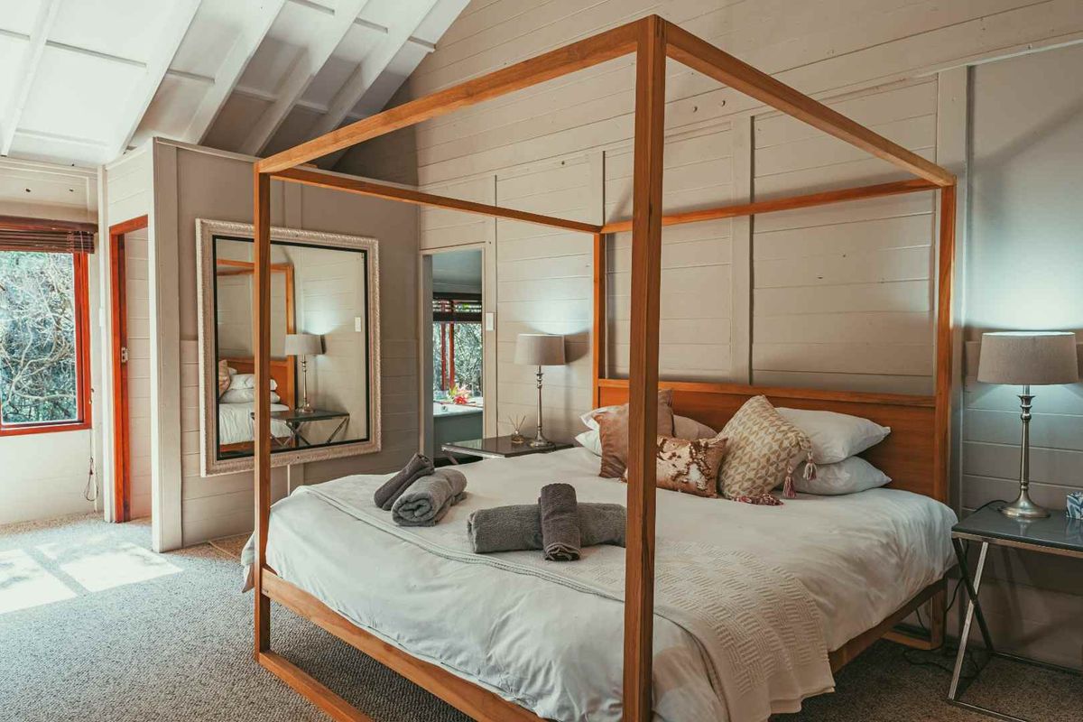 A spacious bedroom featuring vaulted ceilings, timber wall paneling, and large windows that provide natural light and views of the surrounding greenery.