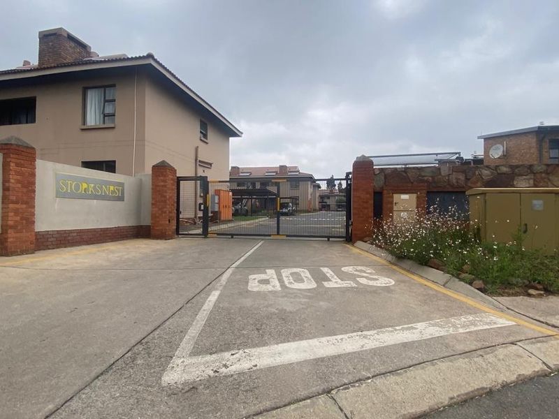 The main entrance to the Storks Nest apartment complex, featuring a secure gated access point, concrete driveway, and brick boundary walling.