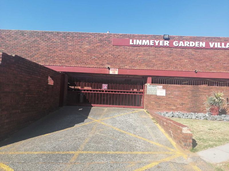 Front entrance view of Linmeyer Garden Villas featuring a brick facade, secure gated driveway access, and exterior security lighting.