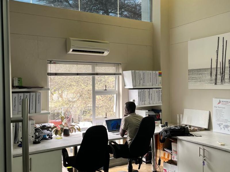 A bright, modern office space featuring polished concrete floors, built-in desk and cabinetry, and large windows providing ample natural light.