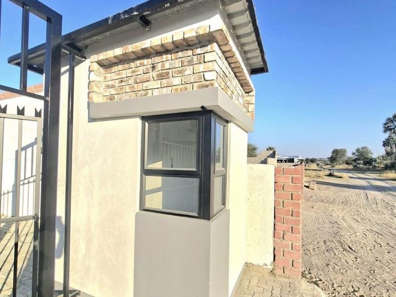 A functional security guard house located at the property entrance, featuring brick detailing, aluminum window frames, and a paved driveway approach.