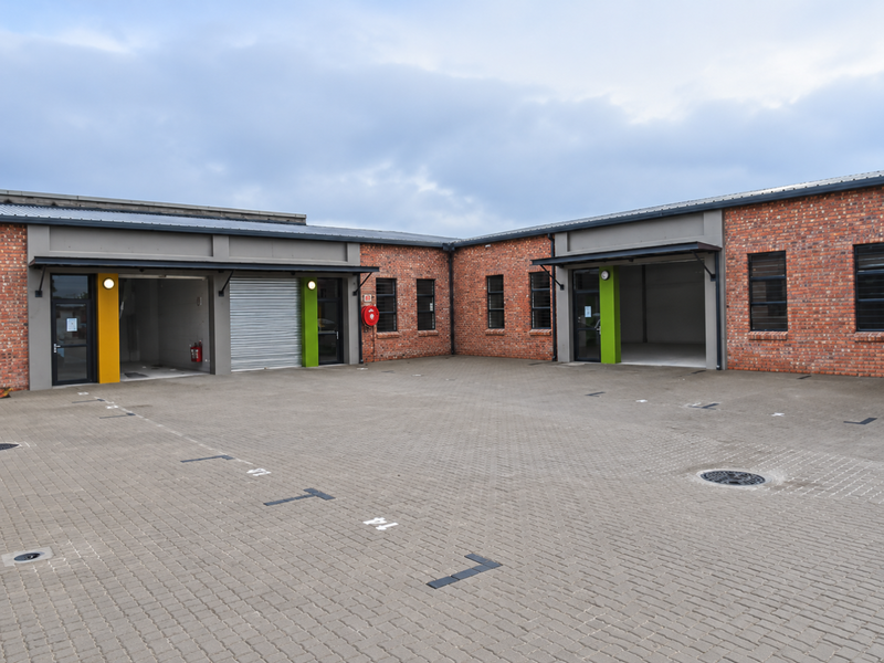 Modern industrial unit complex featuring exposed brick facades, roller shutter doors, and a spacious paved parking courtyard.