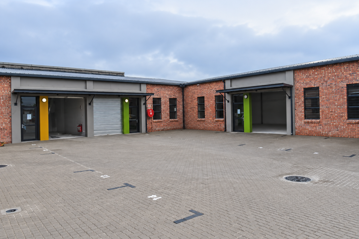Modern industrial unit complex featuring exposed brick facades, roller shutter doors, and a spacious paved parking courtyard.