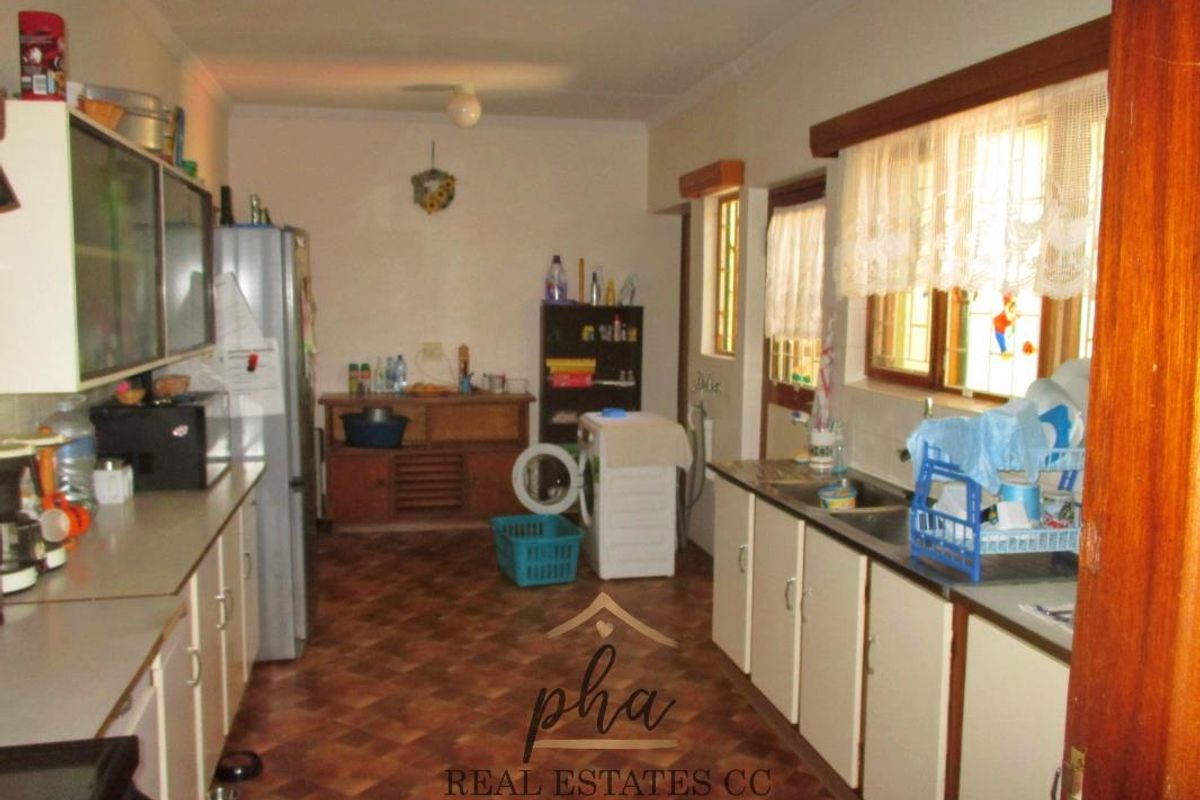 A functional kitchen featuring original cabinetry, laminate countertops, and a double basin sink, offering potential for modernization and layout optimization.
