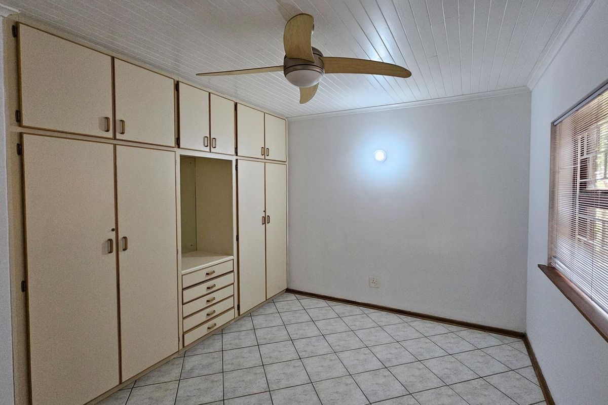 A bedroom featuring extensive built-in cabinetry, tiled flooring, a ceiling fan, and a window with fitted blinds.