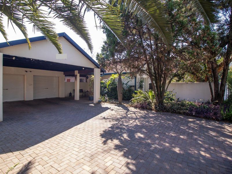 A well-maintained front exterior featuring a paved driveway, a double garage, and a covered carport area with established garden landscaping.