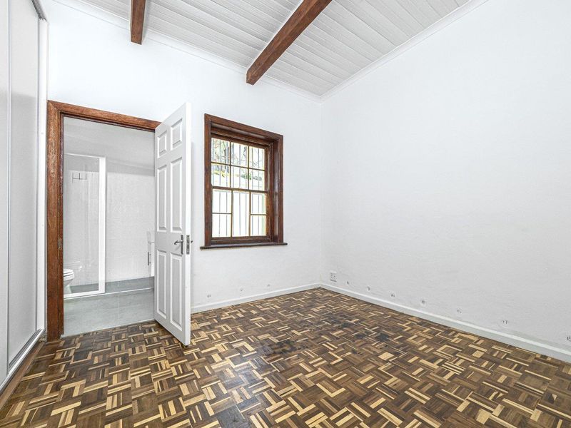 Empty bedroom featuring parquet flooring, exposed timber ceiling beams, and an en-suite bathroom access point.