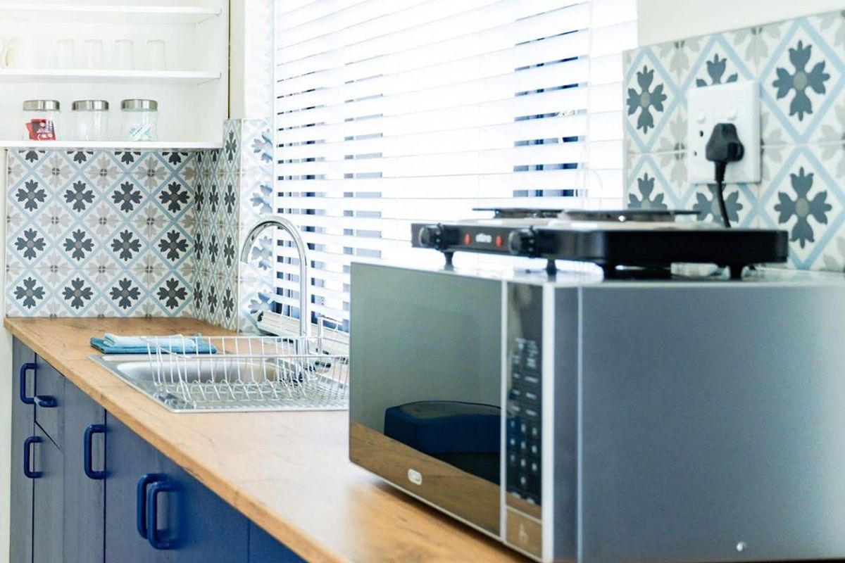 A modern kitchen area featuring blue cabinetry, wooden countertops, patterned tile backsplash, and a stainless steel sink with a window view.