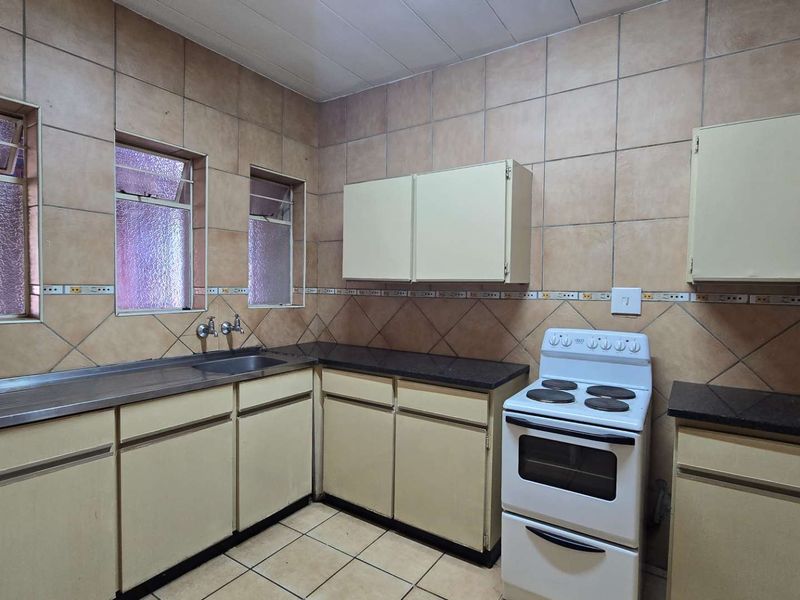 A functional kitchen featuring dated cabinetry, tiled walls, and a stainless steel sink, offering potential for a modern renovation.