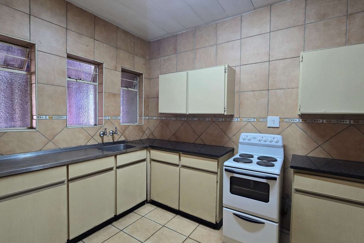 A functional kitchen featuring dated cabinetry, tiled walls, and a stainless steel sink, offering potential for a modern renovation.