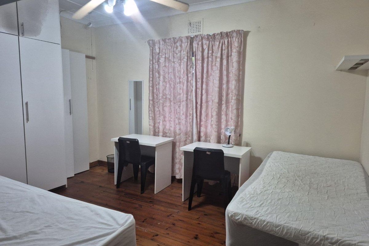 A functional bedroom featuring timber flooring, built-in cupboards, and a ceiling fan, offering a practical layout with natural light.