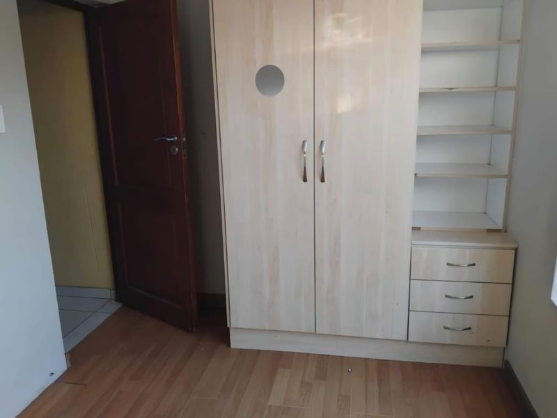A bedroom featuring light wood-tone laminate flooring and a built-in wardrobe with integrated shelving and drawers.