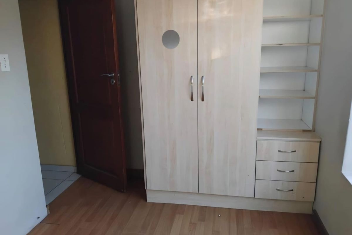 A bedroom featuring light wood-tone laminate flooring and a built-in wardrobe with integrated shelving and drawers.