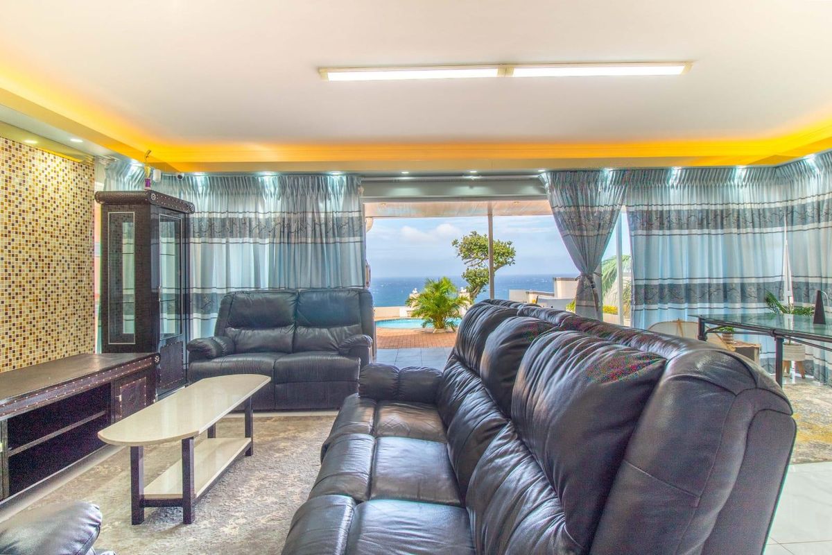 Spacious living room featuring a mosaic tile accent wall, recessed lighting, and large sliding glass doors opening to an outdoor patio with ocean views.