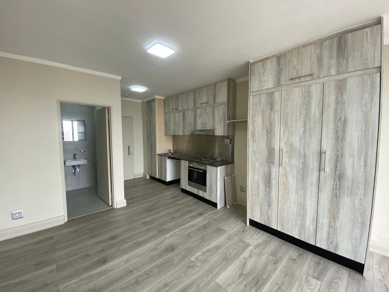 Modern open-plan kitchen area featuring light wood-grain cabinetry, integrated appliances, and durable laminate flooring, leading into a clean, neutral living space.